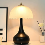 Lampe sans fil Maiori allumée sur une commode, dôme de verre festonné et pied noir galbé